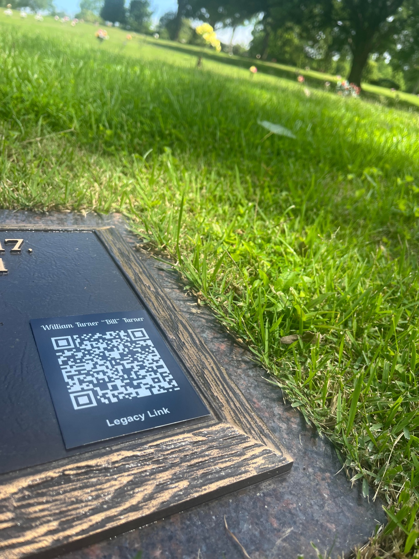 Legacy Link QR memorial plaque set in a bronze grave marker in a sunlit cemetery garden